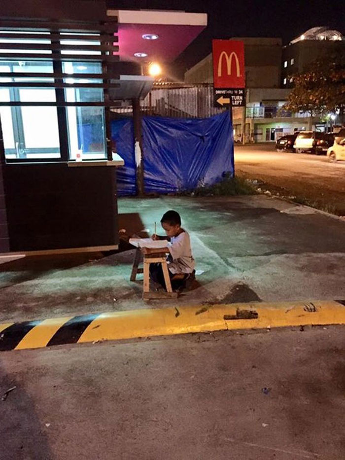 Este niño indigente hace los deberes en la calle a la luz de un McDonalds