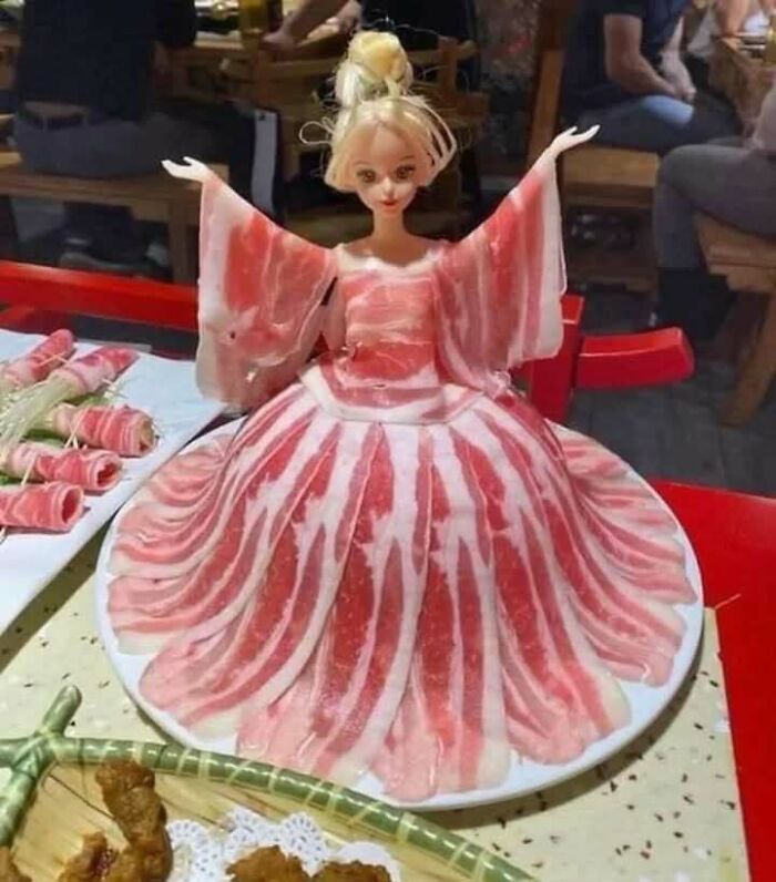 Muñeca con vestido hecho de tocino, representando comida caótica en una mesa de restaurante.