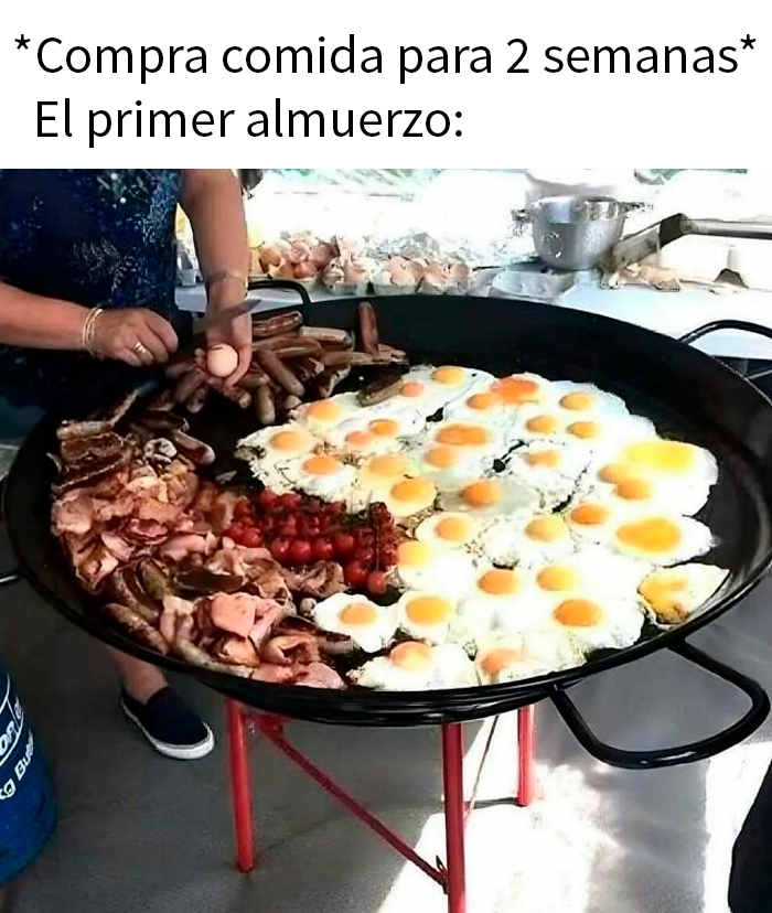 Persona cocinando comida caótica, incluyendo salchichas y huevos fritos, en una gran sartén al aire libre.