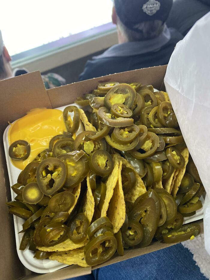 Nachos cubiertos con muchas rodajas de jalapeños, mostrando personas que pidieron algo y se alegraron mucho al recibirlo.