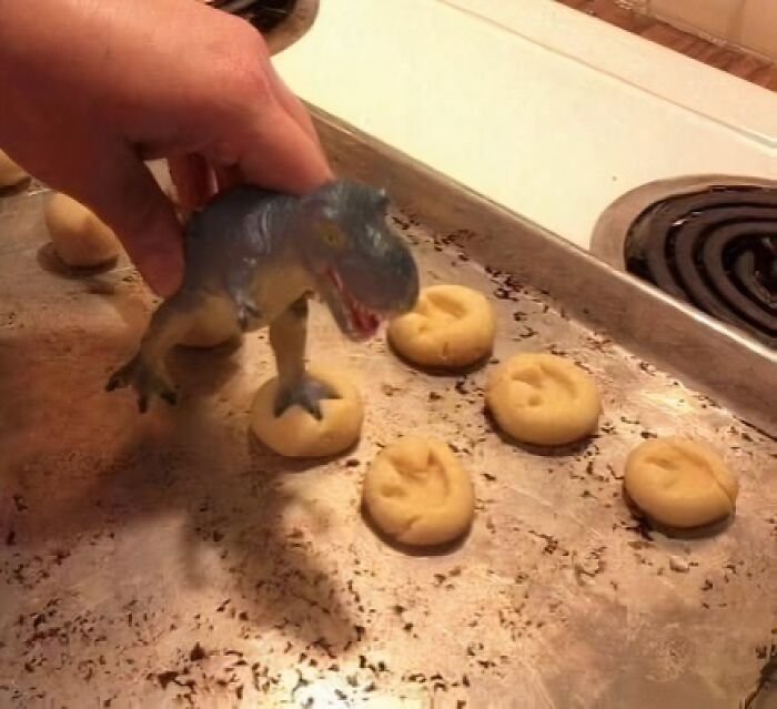 Mano sosteniendo dinosaurio de juguete sobre galletas en bandeja, imagen divertida para memes sobre ciencia y humor.