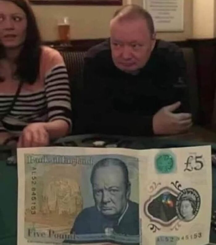 Hombres y mujer en pub británico con imagen divertida y fuera de contexto mostrando billete de cinco libras.