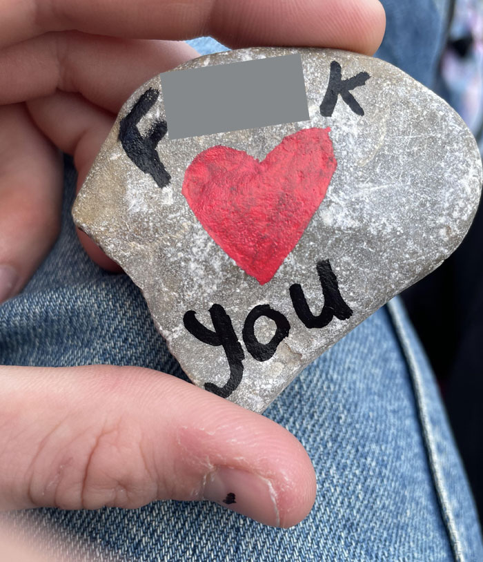 Mano sosteniendo piedra pintada con corazón rojo y texto relacionado con citas que no salieron bien, compartida en internet.
