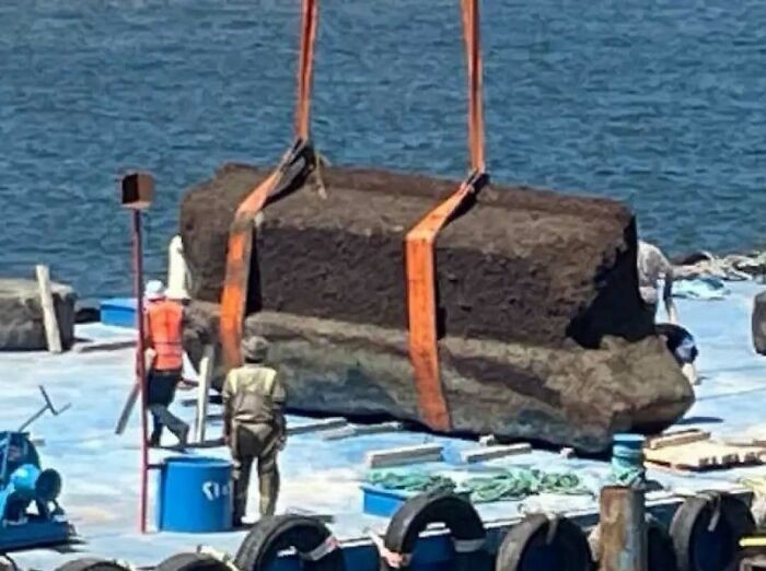 Bloque de piedra gigante siendo izado en puerto, relacionado con datos históricos interesantes y hallazgos arqueológicos.