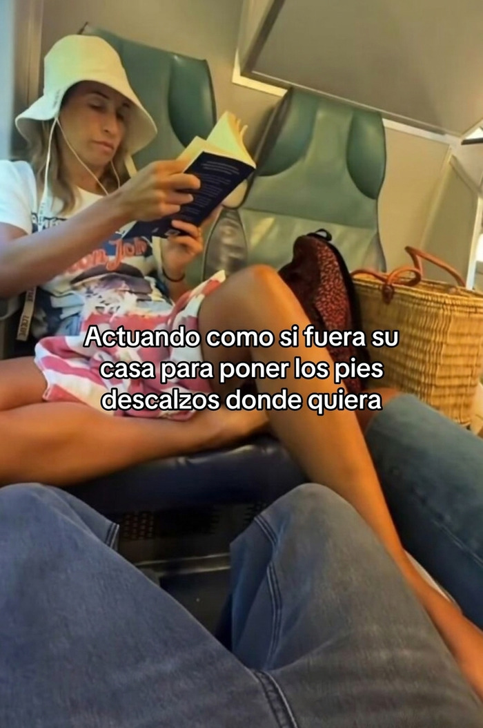 Pasajera egocéntrica con sombrero leyendo un libro y colocando sus pies descalzos sobre otro asiento.