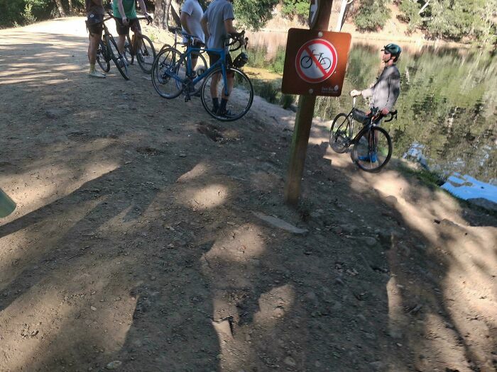 Ciclistas egocéntricos ignorando una señal que prohíbe el paso de bicicletas junto a un lago.