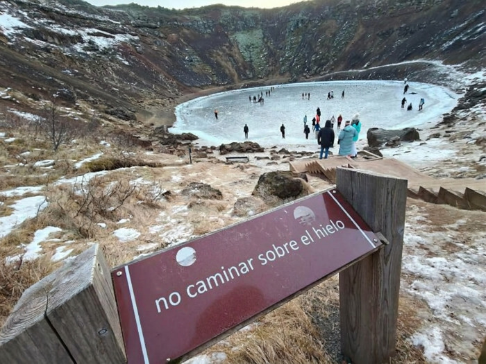 Letrero que prohíbe caminar sobre el hielo con un grupo de personas egocéntricas ignorando la advertencia al fondo.