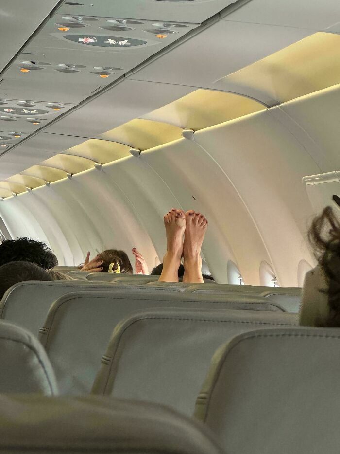 Pasajera egocéntrica con los pies descalzos apoyados sobre el asiento delantero de un avión