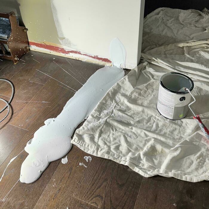 Pintura blanca derramada sobre el suelo de madera junto a una lona, un desastre de que siempre puede empeorar.