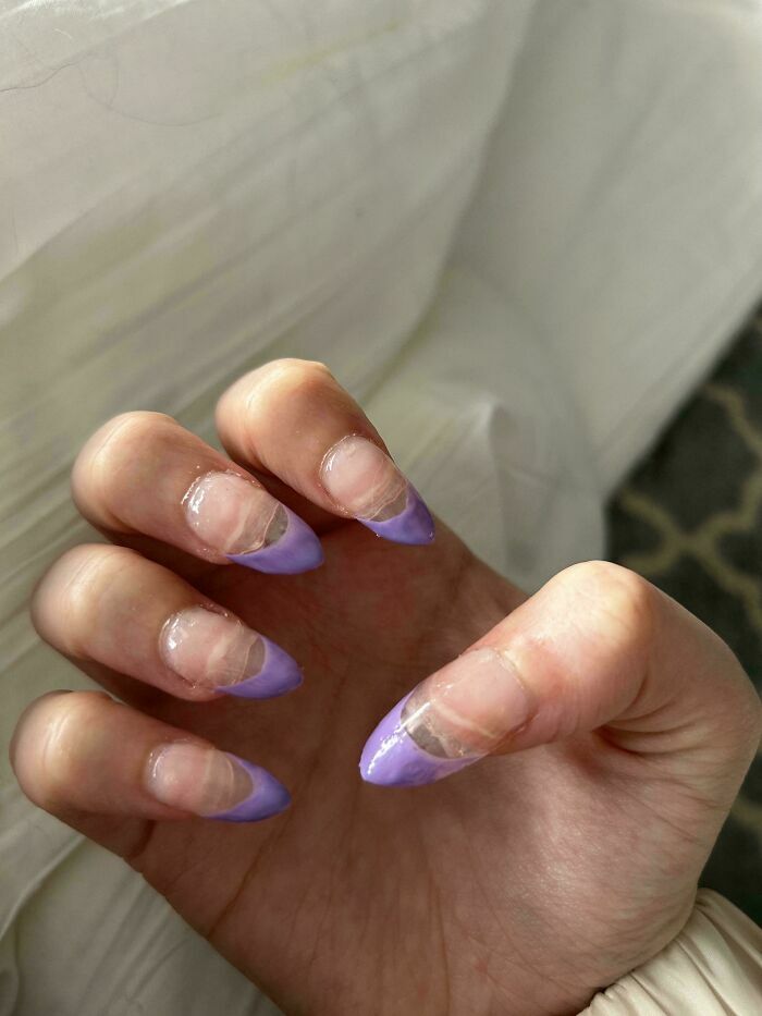 Mano mostrando unas uñas mal pintadas de color morado tras una mala sesión en el salón de belleza.