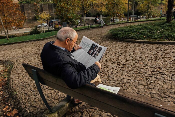 Hombre mayor leyendo el periódico impreso en el parque, representando industrias tradicionales a punto de colapsar