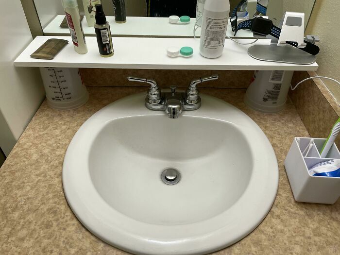 Repisa blanca de baño sostenida por dos vasos de plástico boca abajo, fallando en proyectos caseros.