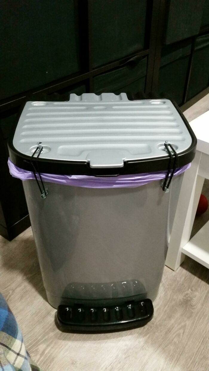 Bote de basura gris con tapa asegurada por ligas negras, parte de proyectos caseros peculiares.