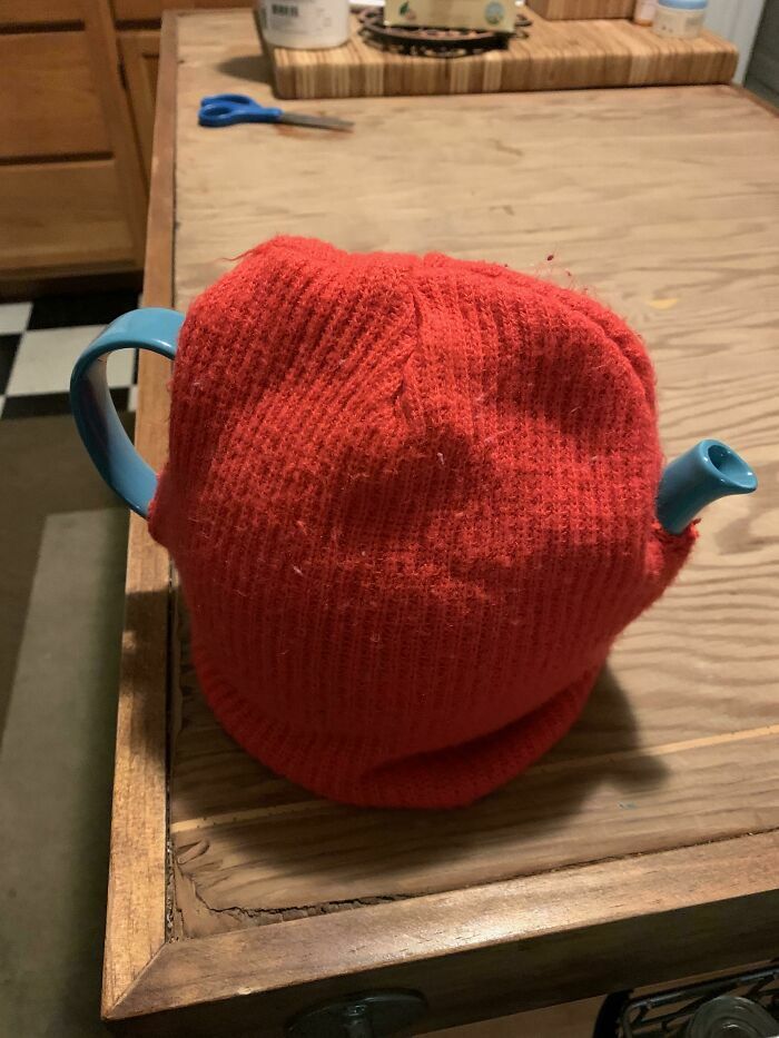 Tetera azul cubierta con un gorro de lana rojo como calentador improvisado en proyectos caseros.