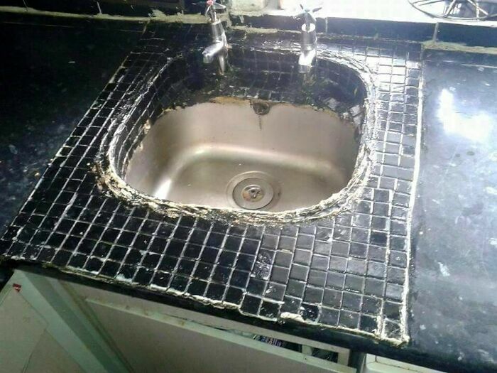Fregadero mal sellado con azulejos negros desalineados en proyectos caseros defectuosos.