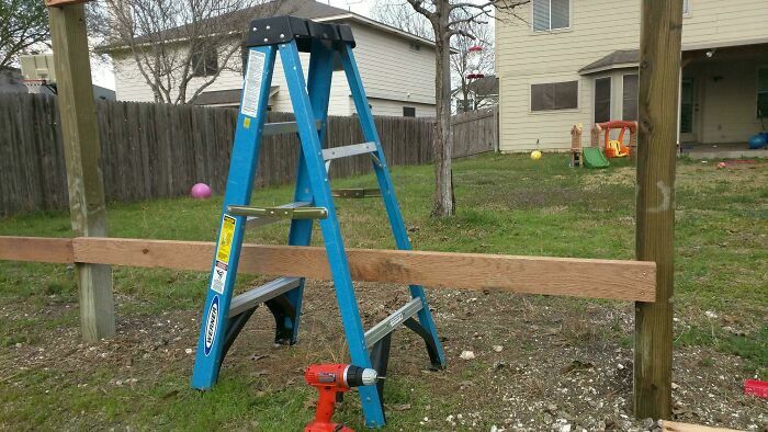 Escalera azul atrapada bajo valla de madera, errores en proyectos caseros.