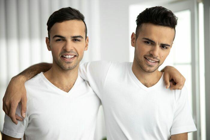 Dos hombres jóvenes sonrientes con camisetas blancas que parecen gemelos