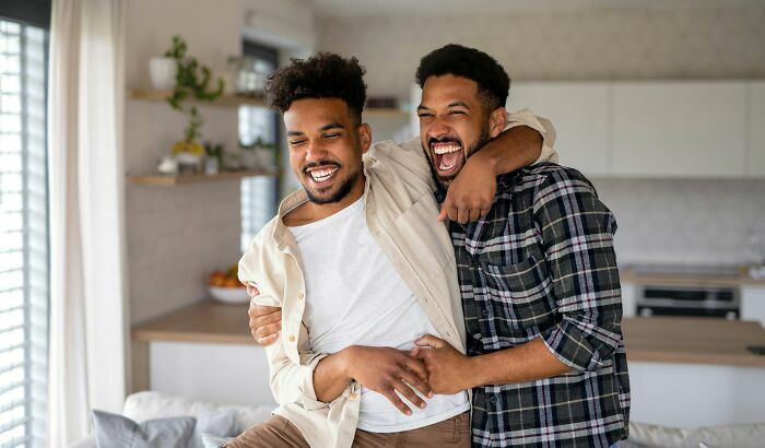 Dos amigos o gemelos abrazándose de manera divertida en casa mientras ríen alegremente