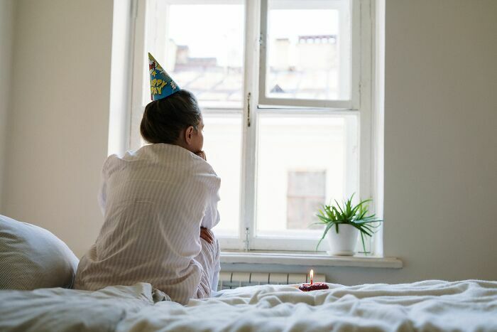 Una mujer de espaldas mirando por la ventana en su cumpleaños con un gorrito festivo