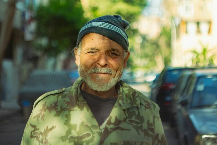Un hombre mayor sonriente en la calle con gorro de lana, compartiendo sus historias de vida.