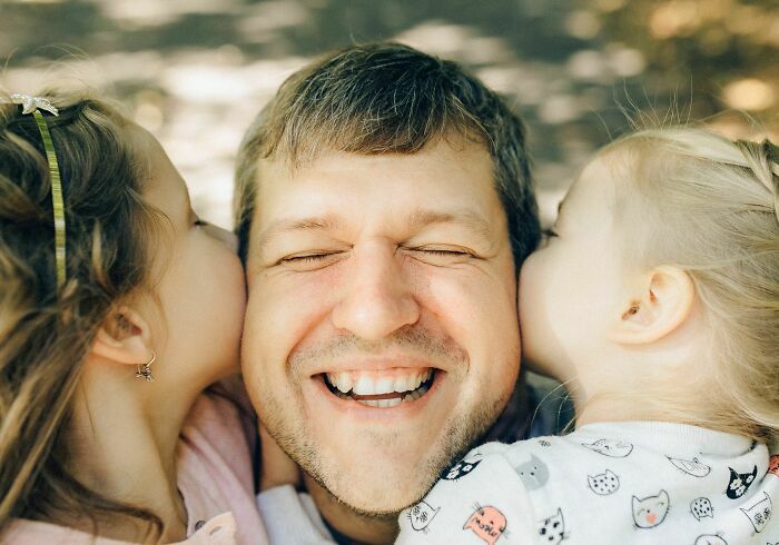 Un padre sonriente abrazando a sus hijas, un ejemplo de hermosas historias familiares.