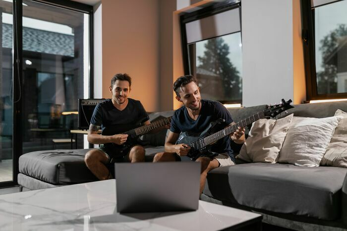 Dos hermanos gemelos sentados en el sofá de su casa tocando la guitarra eléctrica