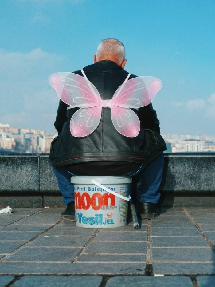 Un hombre con alas de mariposa rosa en escenas callejeras curiosas.