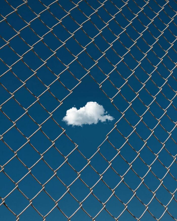 Nube blanca enmarcada en el hueco de una cerca, una creativa escena callejera urbana.