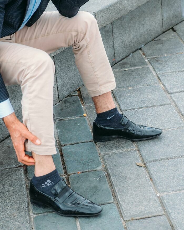 Fotografía callejera curiosa de persona con mocasines negros y calcetines de marcas deportivas diferentes.