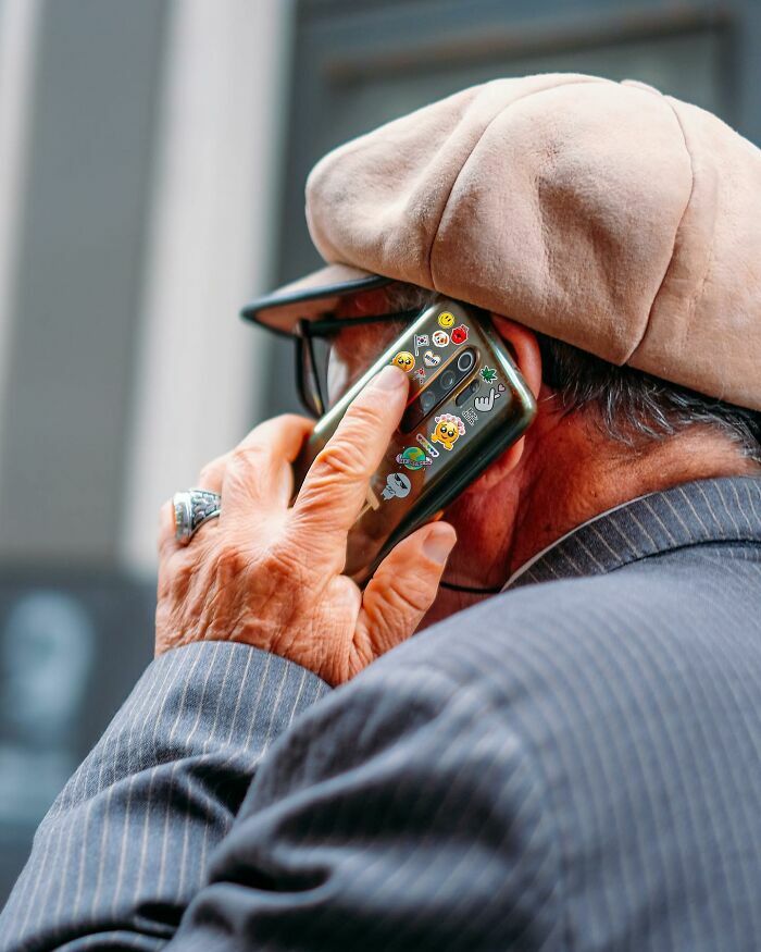 Hombre mayor hablando por teléfono móvil decorado con pegatinas en una escena callejera.