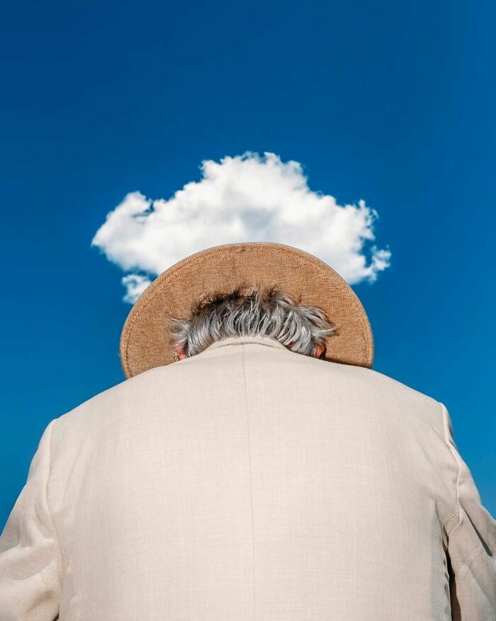 Fotografía callejera de persona con sombrero alineado perfectamente con una nube en el cielo azul.