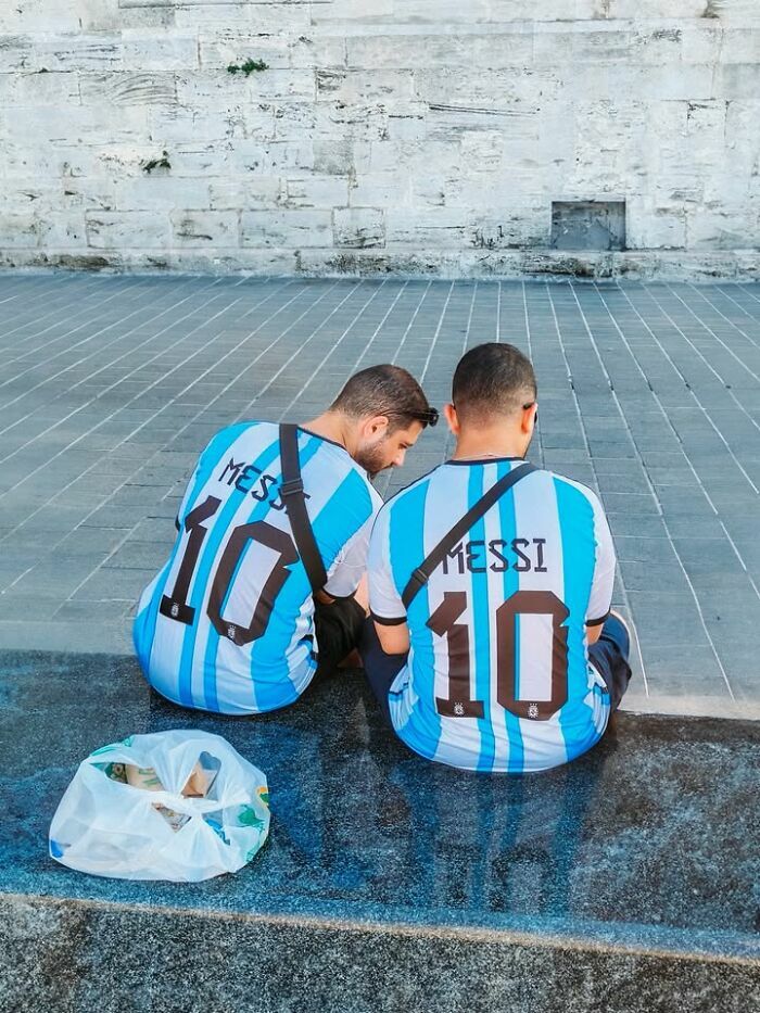 Dos hombres con camisetas de Messi sentados juntos en curiosas escenas callejeras con sincronización tan perfecta.