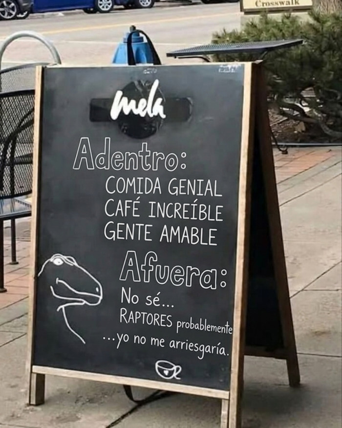 Pizarra callejera con un mensaje de imágenes divertidas sobre dinosaurios en el exterior de una cafetería.