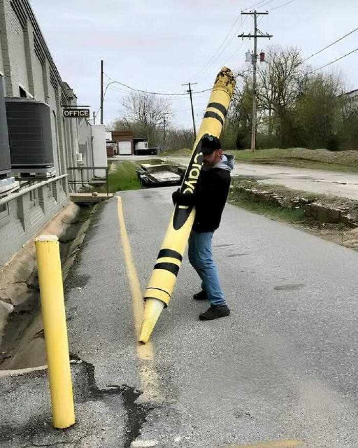 Un hombre usando un crayón gigante amarillo para pintar la línea de la calle en imágenes tan divertidas como disparatadas.