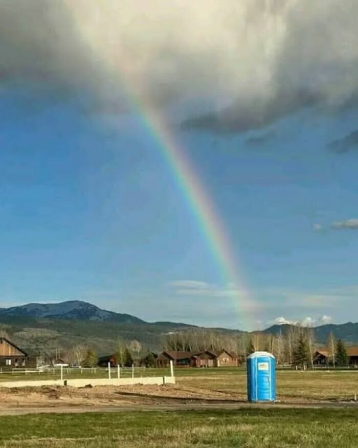 Imágenes divertidas de un arcoíris que termina exactamente sobre un baño portátil azul en un campo
