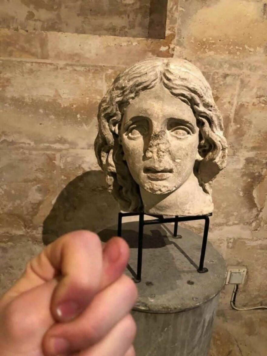 Mano jugando a robar la nariz a una estatua antigua, creando una escena confusa y divertida.