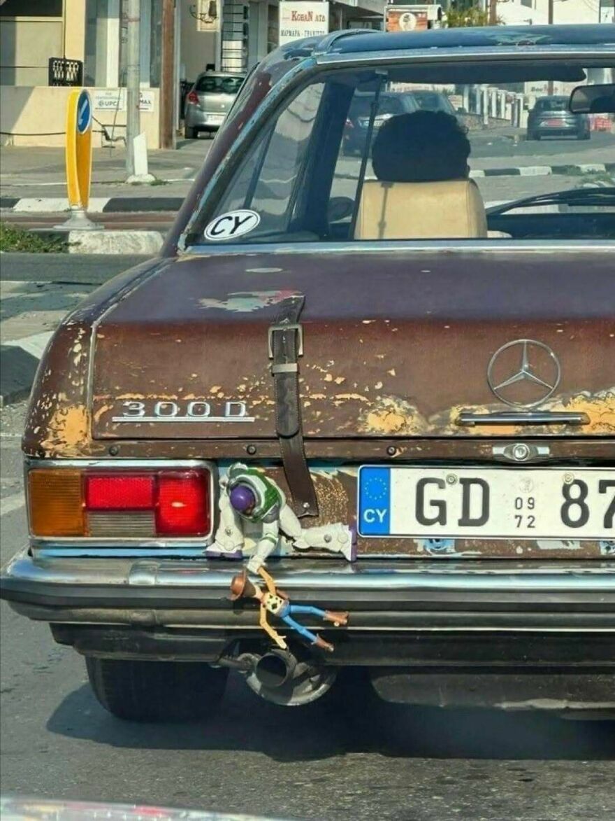 Muñecos de Toy Story colgando del parachoques de un coche viejo en una escena confusa y divertida.