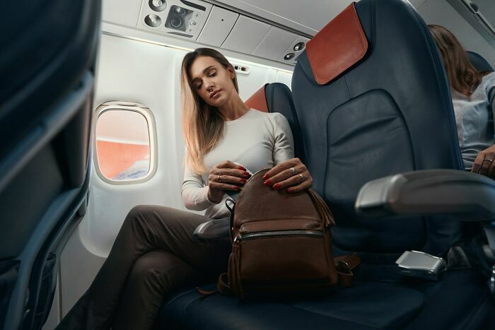 Pasajera acomodando mochila en asiento de avión durante el viaje