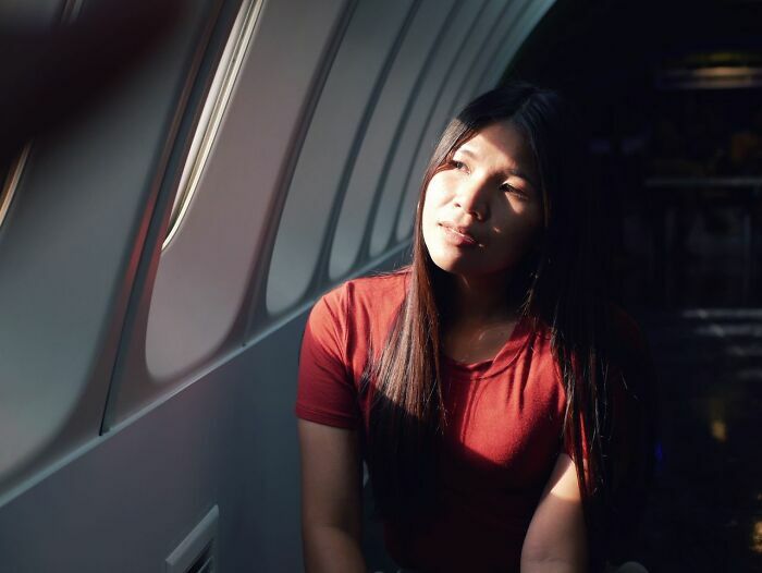 Mujer sentada junto a la ventana en avión pensando en vuelo