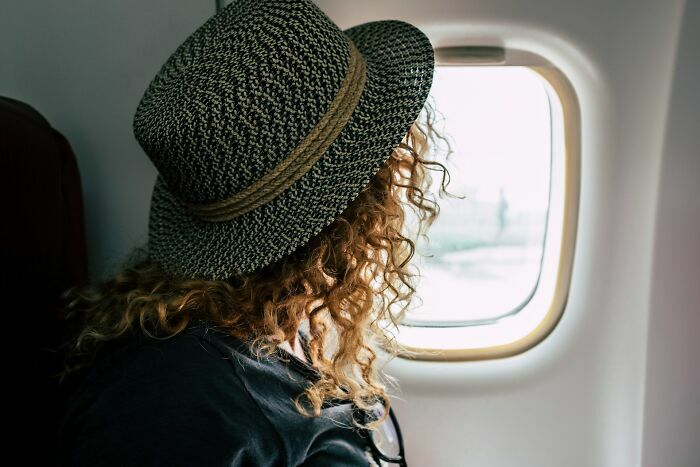 Pasajera con sombrero mirando por ventana de avión en viaje