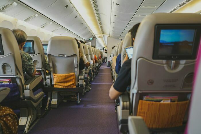Pasajeros sentados en filas con pantallas de entretenimiento en avión