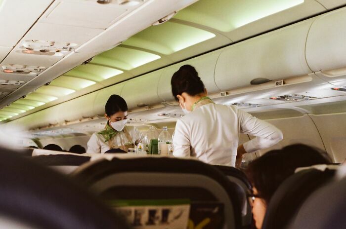 Azafatas atendiendo pasajeros en avión durante servicio a bordo con pasajeros visibles