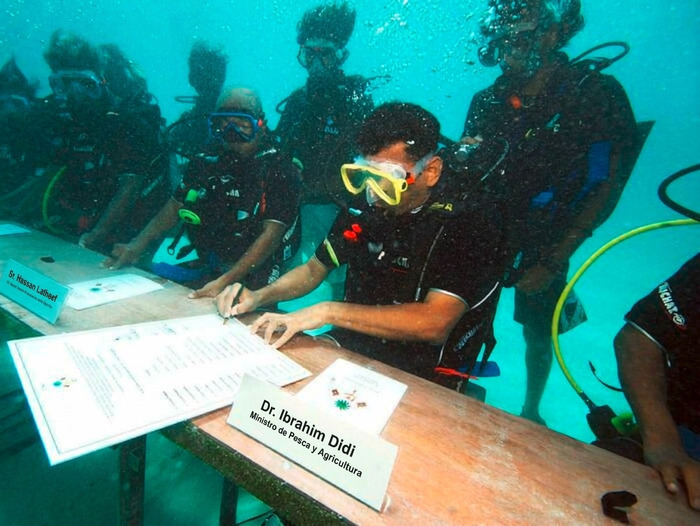 Personas buceando bajo el agua firmando documentos mesa submarina