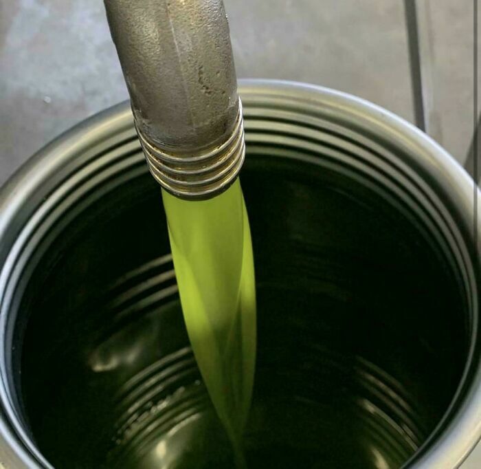 Manguera vertiendo líquido verde dentro de un recipiente metálico