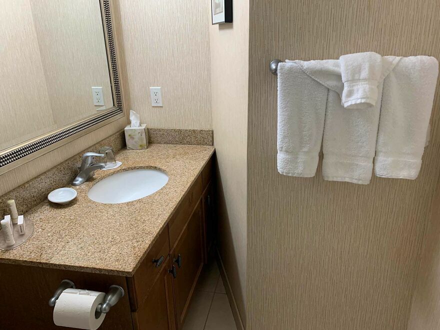 Fallo en hotel mostrando toallas dobladas como un pantalón colgadas en baño pequeño