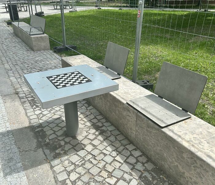 Banco con sillas metálicas incómodas y mesa con tablero de ajedrez
