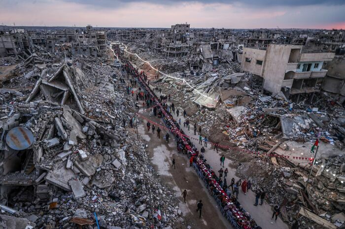 Imagen ganadora de zona destruida por conflicto con fila de personas en ruinas