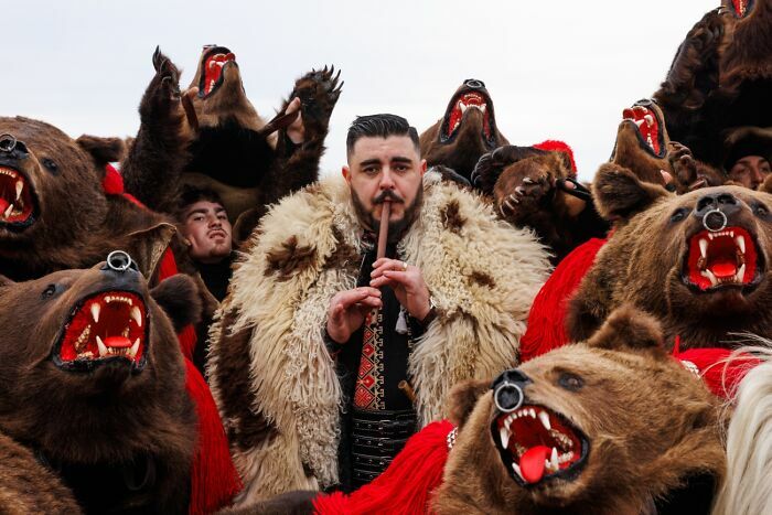Hombre con traje tradicional rodeado de figuras con máscara de oso en los Premios internacionales de fotografía Siena