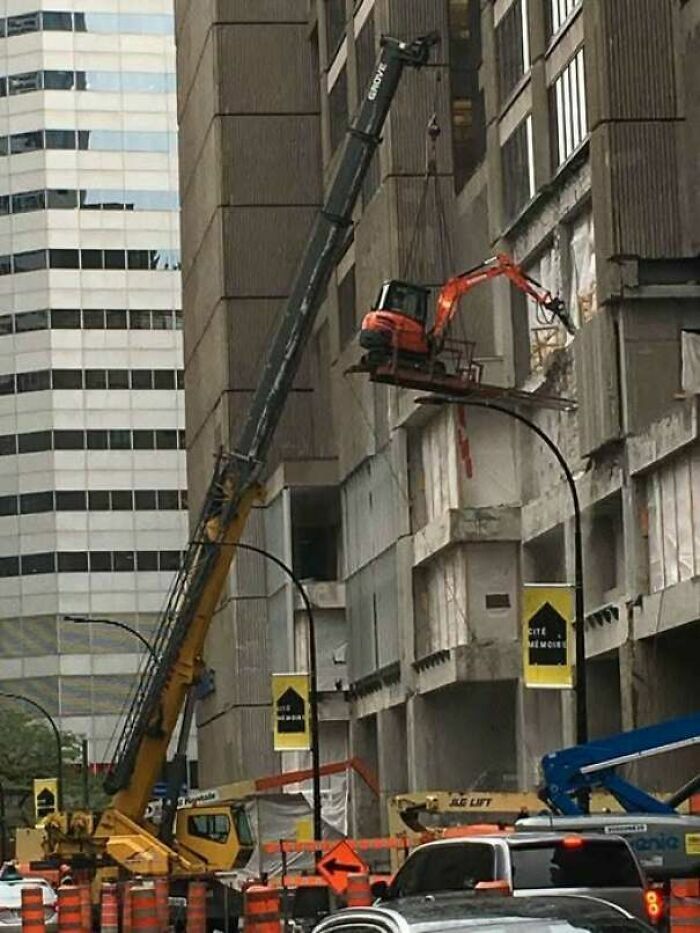 Grúa elevando una excavadora en un edificio con claros fallos de construcción.