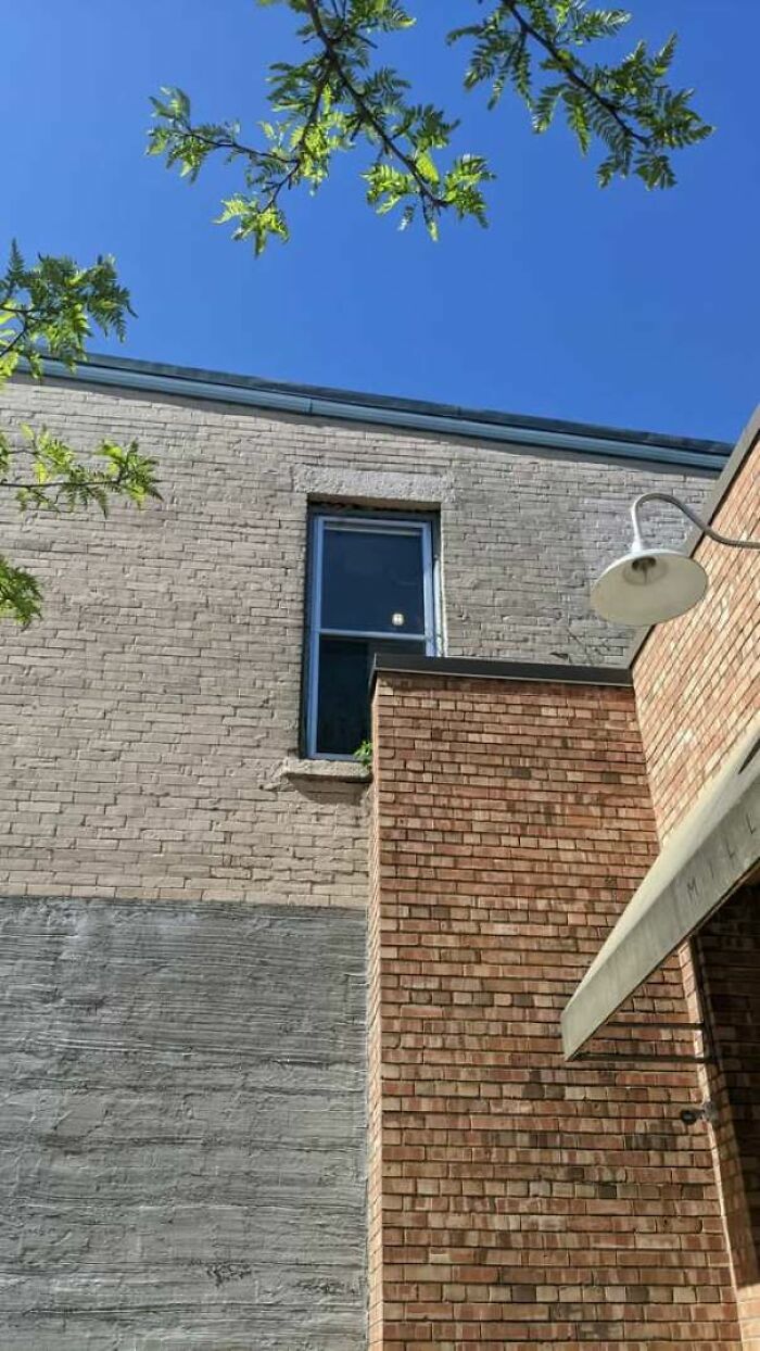 Ventana parcialmente bloqueada por una pared de ladrillo, un claro fallo de construcción en la fachada.